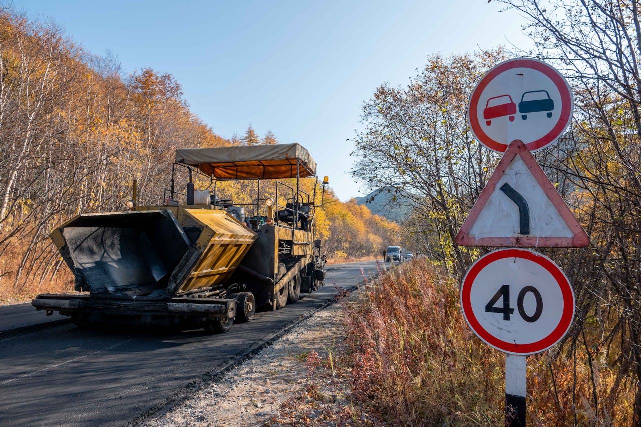 Road construction in autumn with speed limit sign and machinery on a sunny day.