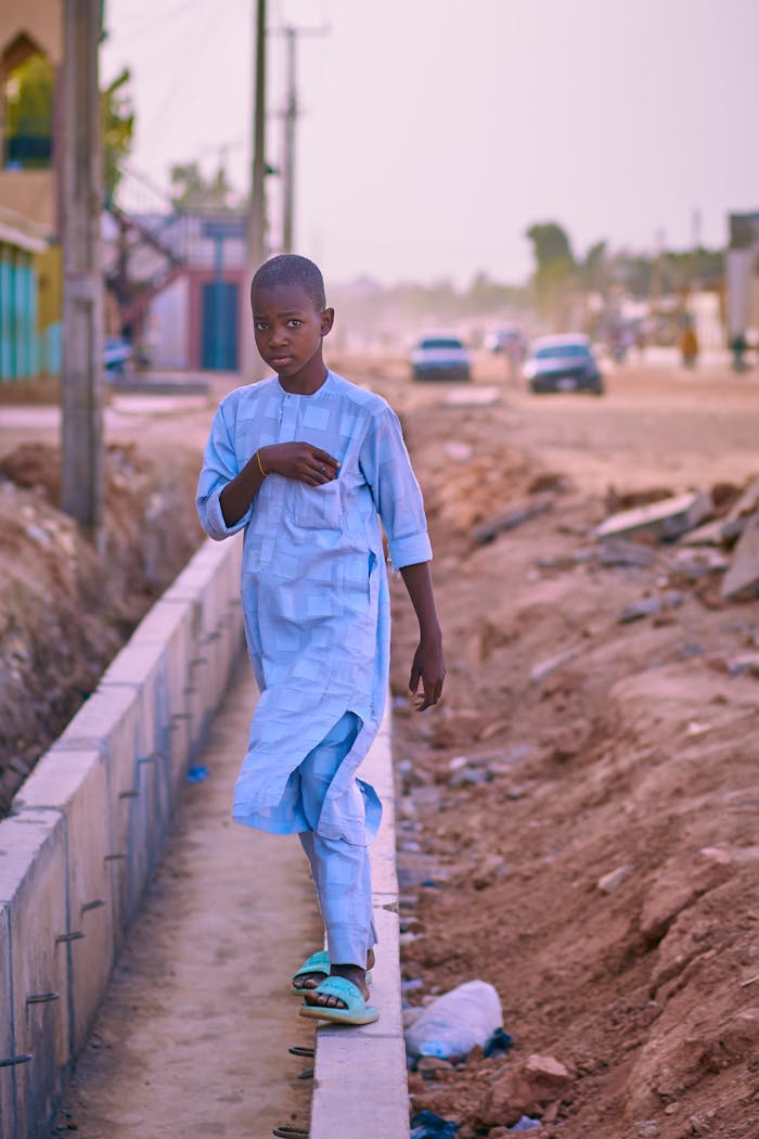 A young boy dressed in traditional attire walks down a street in Nigeria, showing urban life.