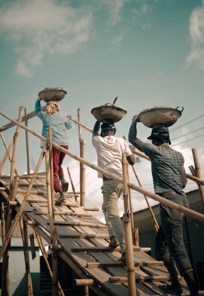 Three men at work carrying materials on a wooden ramp at a construction site in Nigeria.
